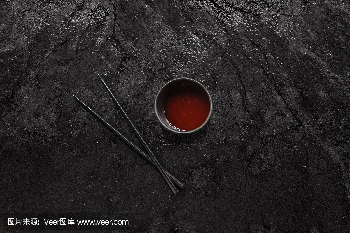 木制的黑色筷子和糖醋汁碗上的黑色石板石。