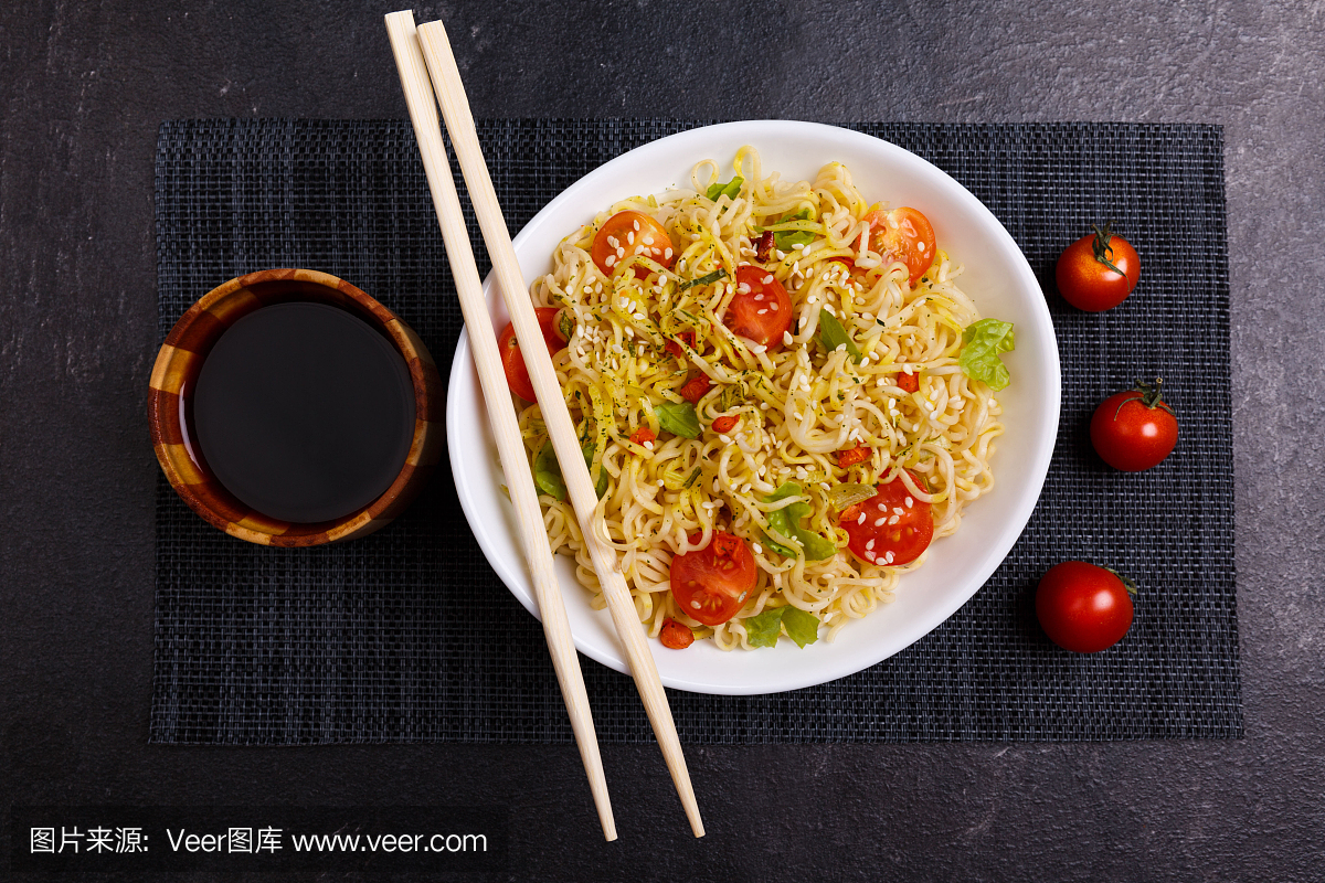 一份开胃的中国面条,上面有西红柿和蔬菜,旁边是西红柿、酱油和筷子。